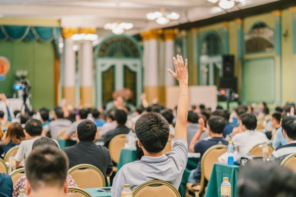 Rear view of Audience showing hand to answer the question from Speaker on the stage